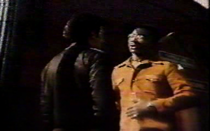 Supposed still frame from Black the Ripper. This apparently shows Mike (black jacket) interrogating a former pimp known as Sideback (orange outfit).
