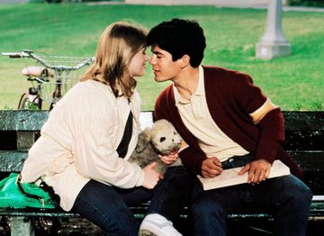 Paul and Samantha kissing on a bench as Samantha holds a small toy.