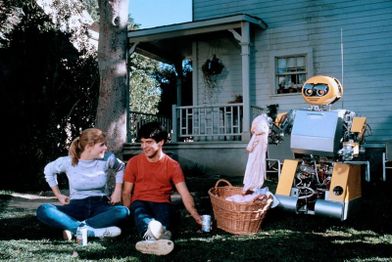 Paul and Samantha sitting in a yard as BB fiddles with laundry.